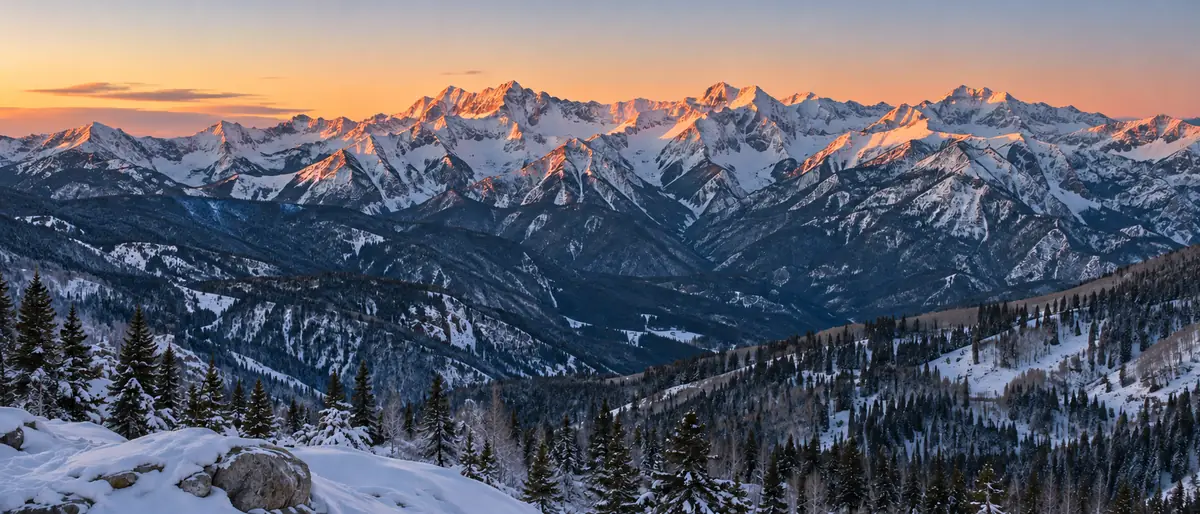 Snowy mountain ridgeline glowing pink and orange at sunrise above a shaded valley